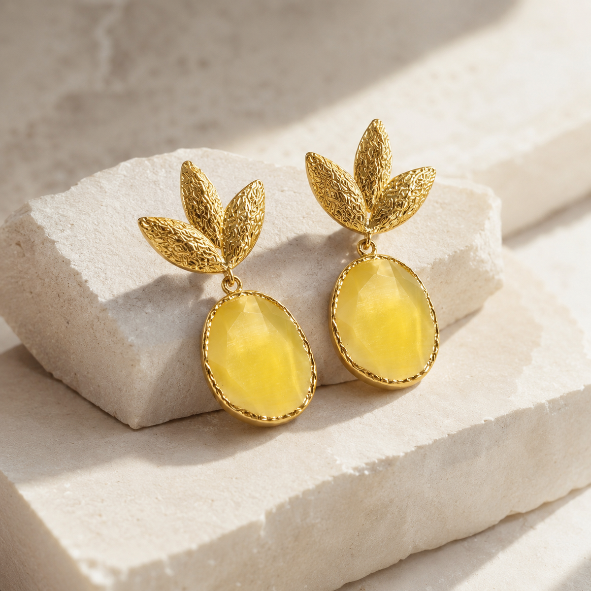 Angled view of textured leaf drop earrings with a mustard yellow oval center.