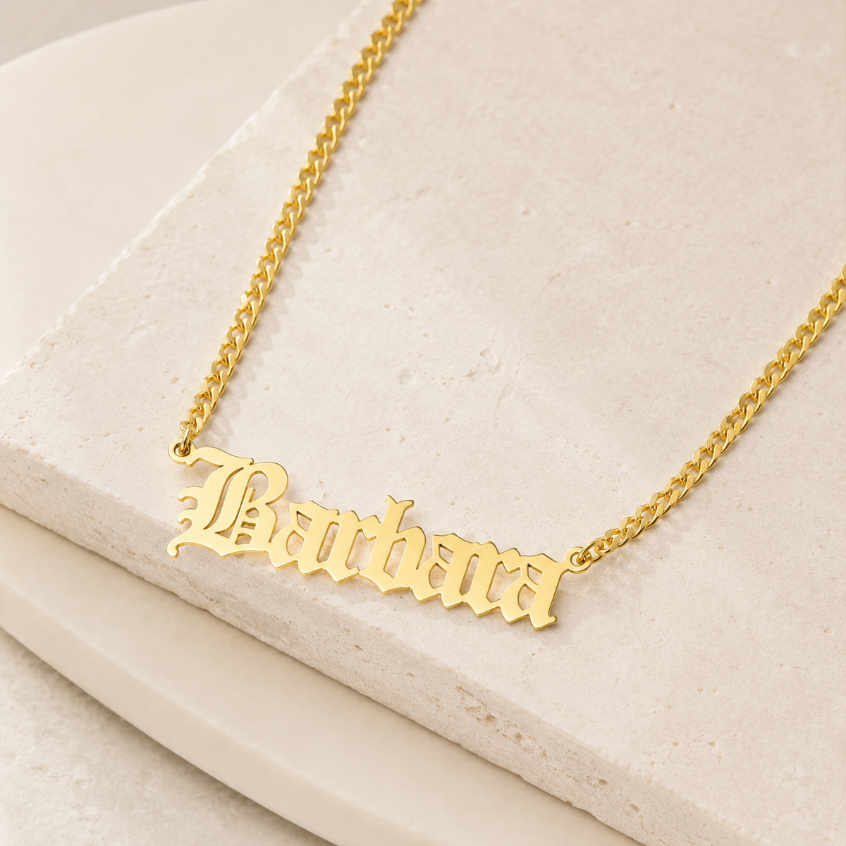 Angled view of a gold-tone engraved name necklace with a classic chain.