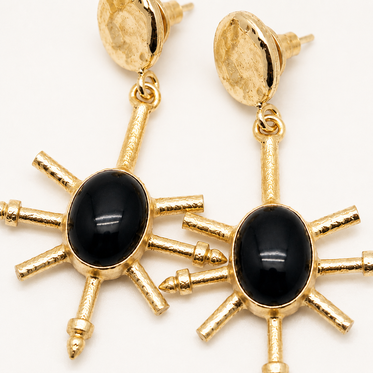 Close-up of gold-plated earrings with black onyx centers and textured spike accents.