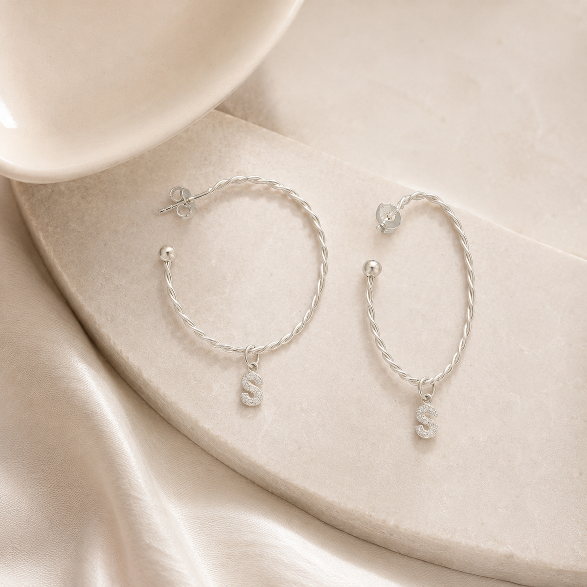 Twisted hoop earrings with a personalized initial charm on a white background.