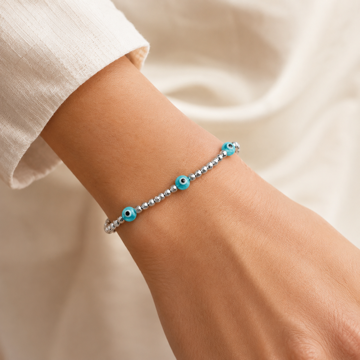 Silver bracelet with three blue evil eye accents shown on a white background.