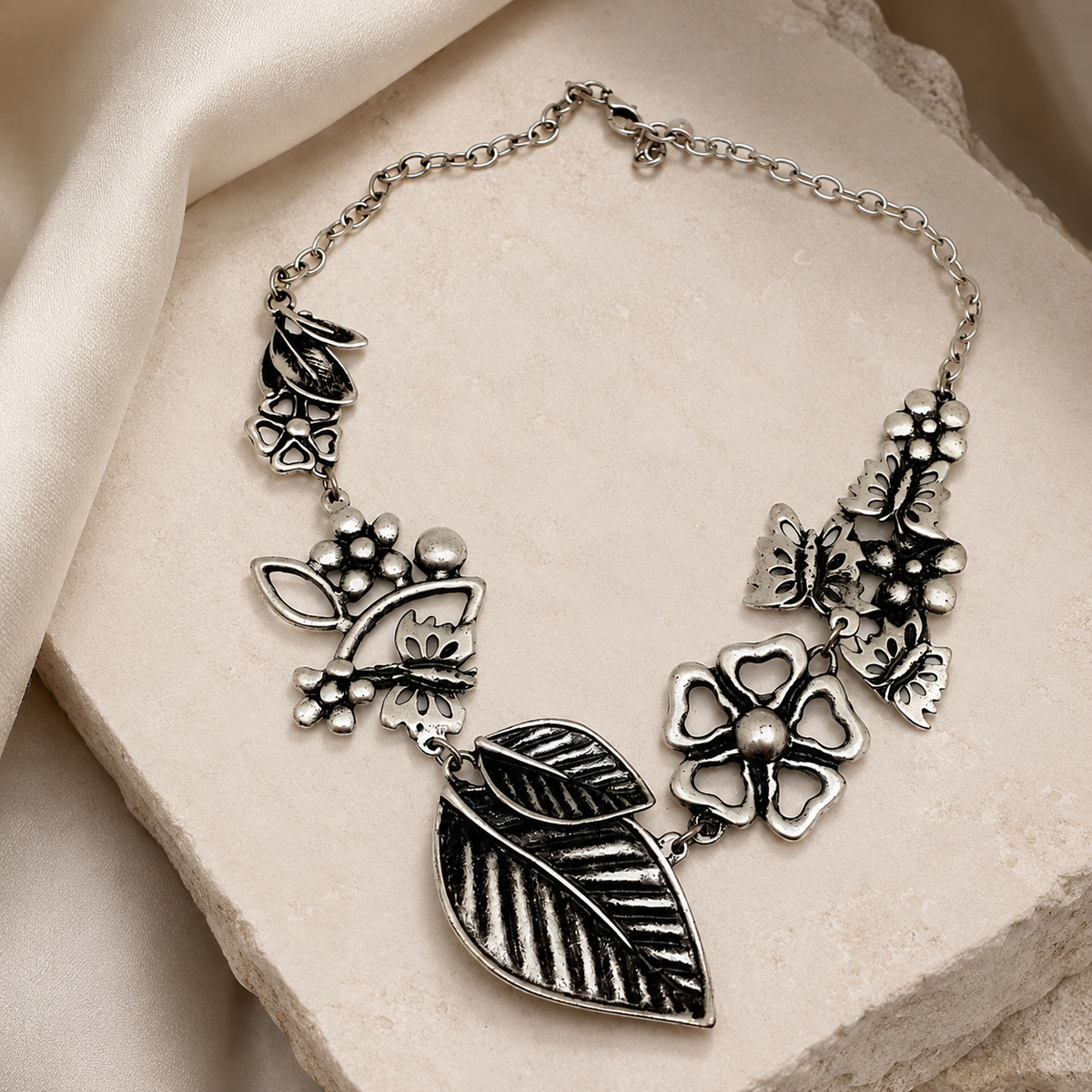Silver-tone statement necklace with layered floral motifs and leaf pendants.