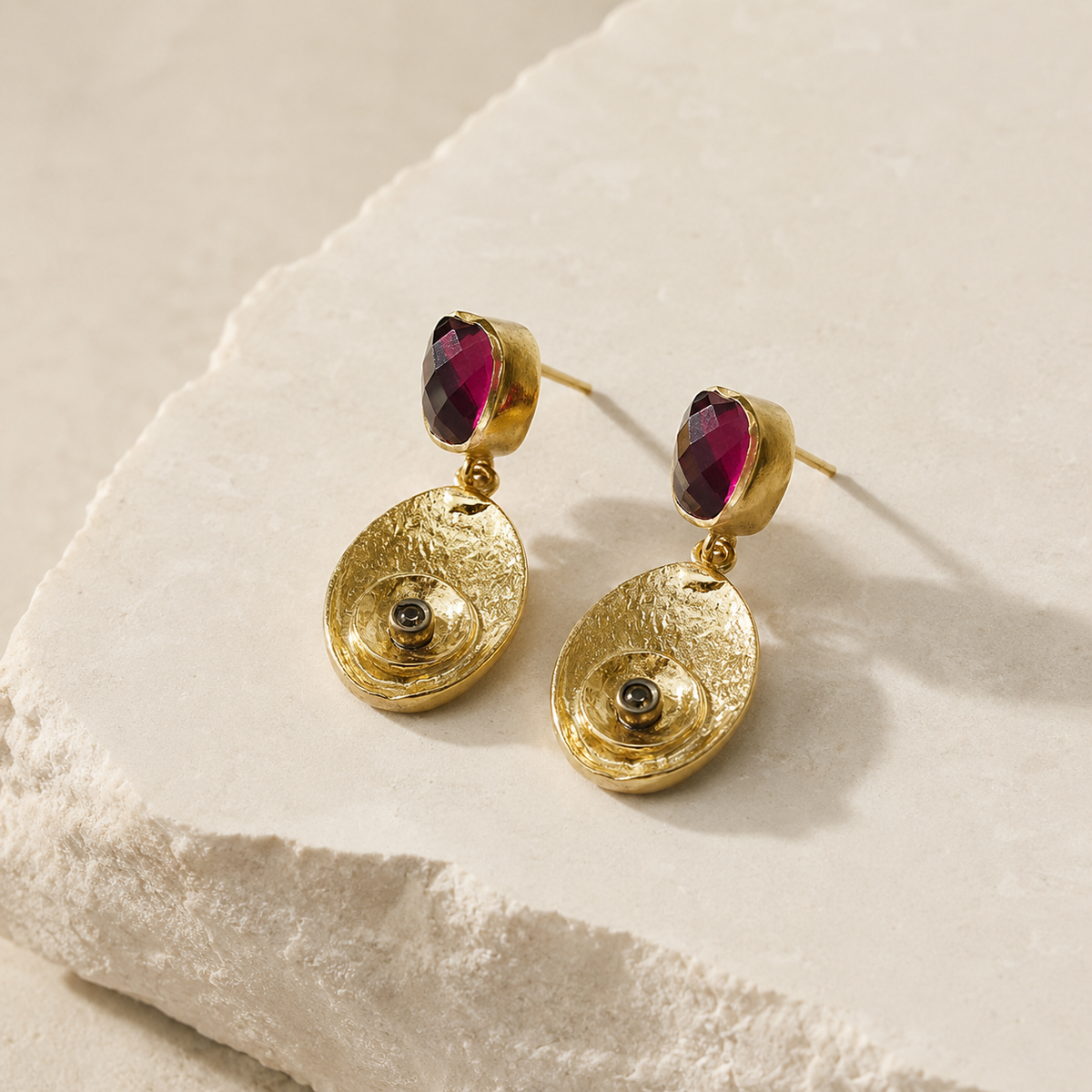 Angled view of gold-plated drop earrings with olive green stones and textured pendants.