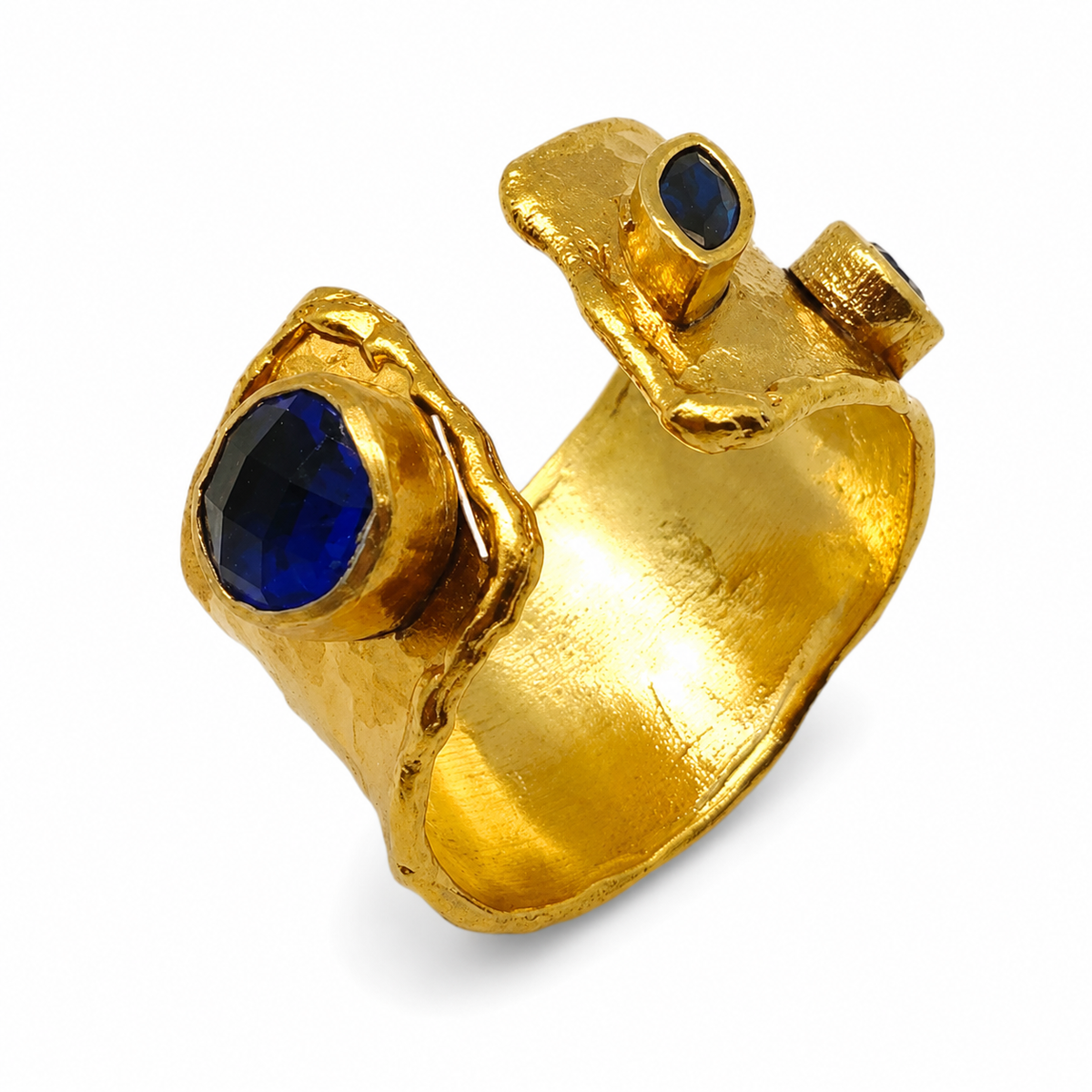 Gold-plated open cuff ring with sapphire blue stones and a textured sculptural shape.
