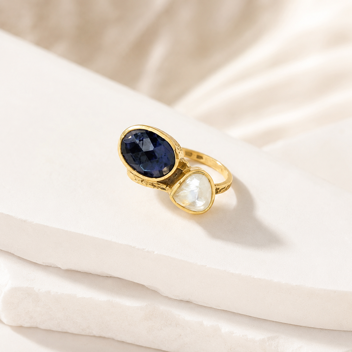 Angle view of a gold-plated ring with navy blue crystal and pearl-like stone.