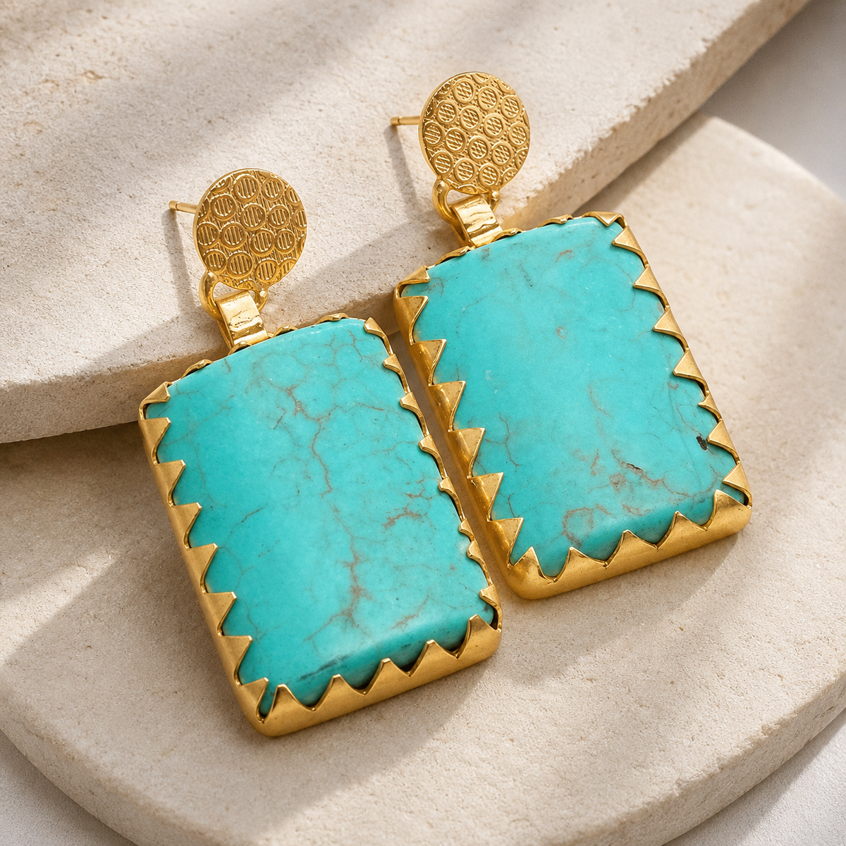Angle view of square turquoise earrings with gold-plated trim and round top accents.