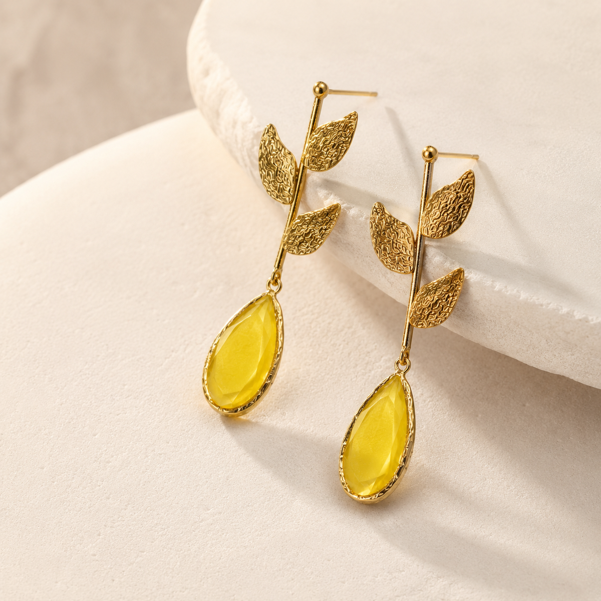 Angle view of gold plated drop earrings with textured leaf details and mustard yellow accents.