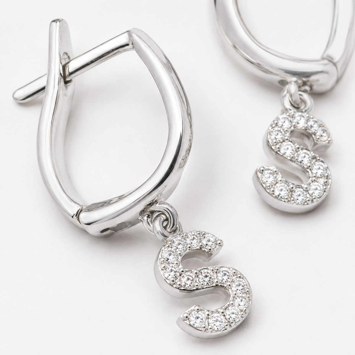 Close-up of a silver-tone huggie earring with CZ initial detail.