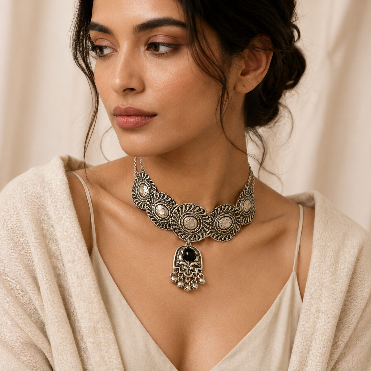 Front view of a silver-tone embossed disc necklace with a black stone pendant.
