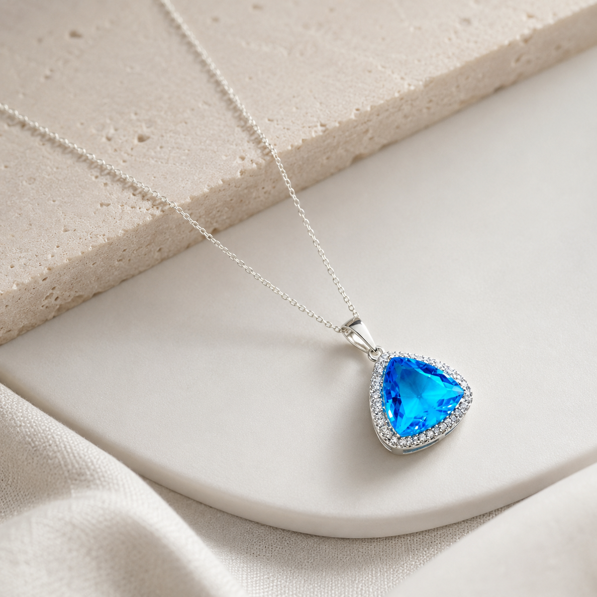 Angle view of a triangle pendant necklace with a baby blue faceted stone.