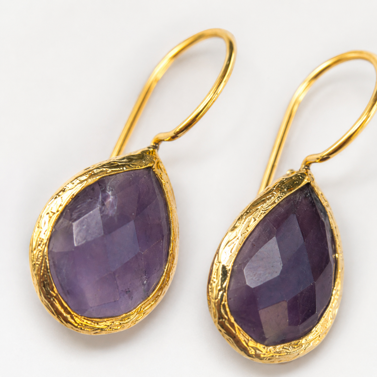 Close view of faceted purple teardrop stones framed in gold-plated metal.