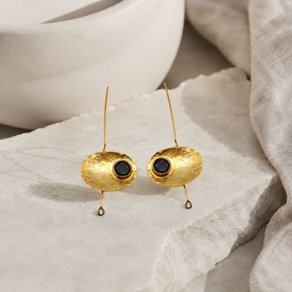Gold-plated oval statement earrings with black stone centers on a white background.