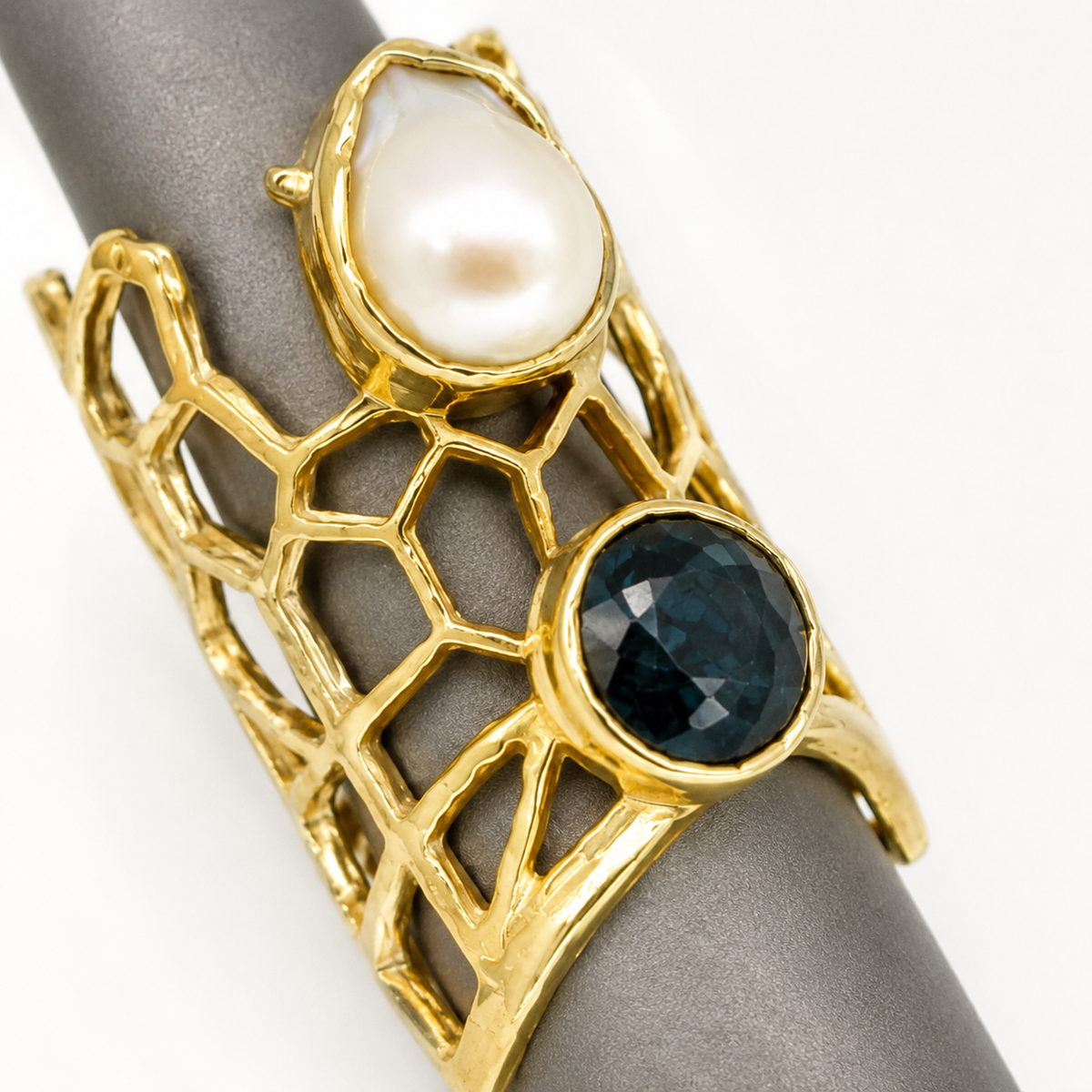 Close view of a gold-plated ring with pearl-like and onyx-style stones in a honeycomb setting.