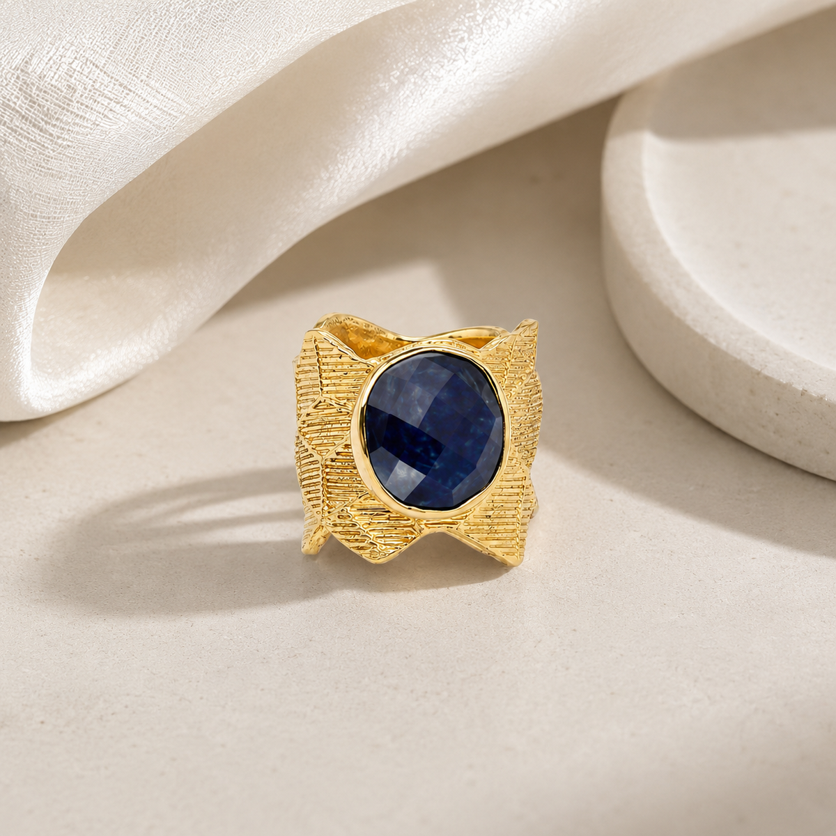 Gold-tone geometric ring with a deep navy oval stone on a white background.