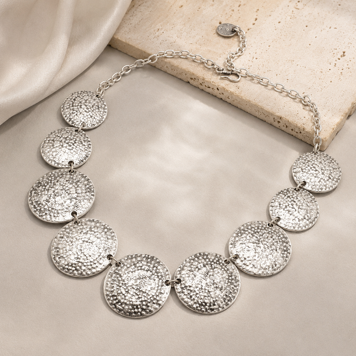 An angled view of the hammered disc necklace with a silver-tone finish.