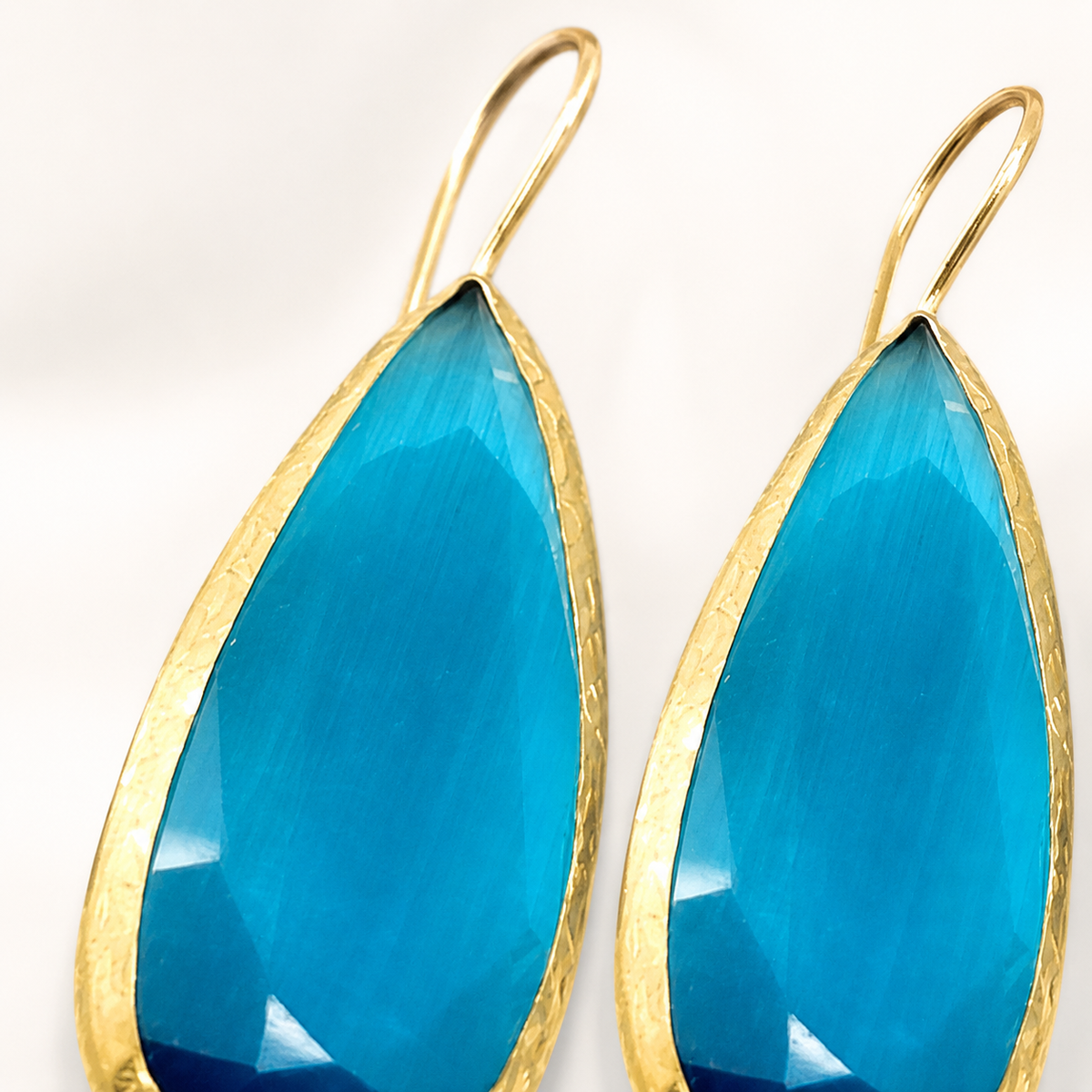 Close-up of faceted blue teardrop earrings with gold-plated brass edges.