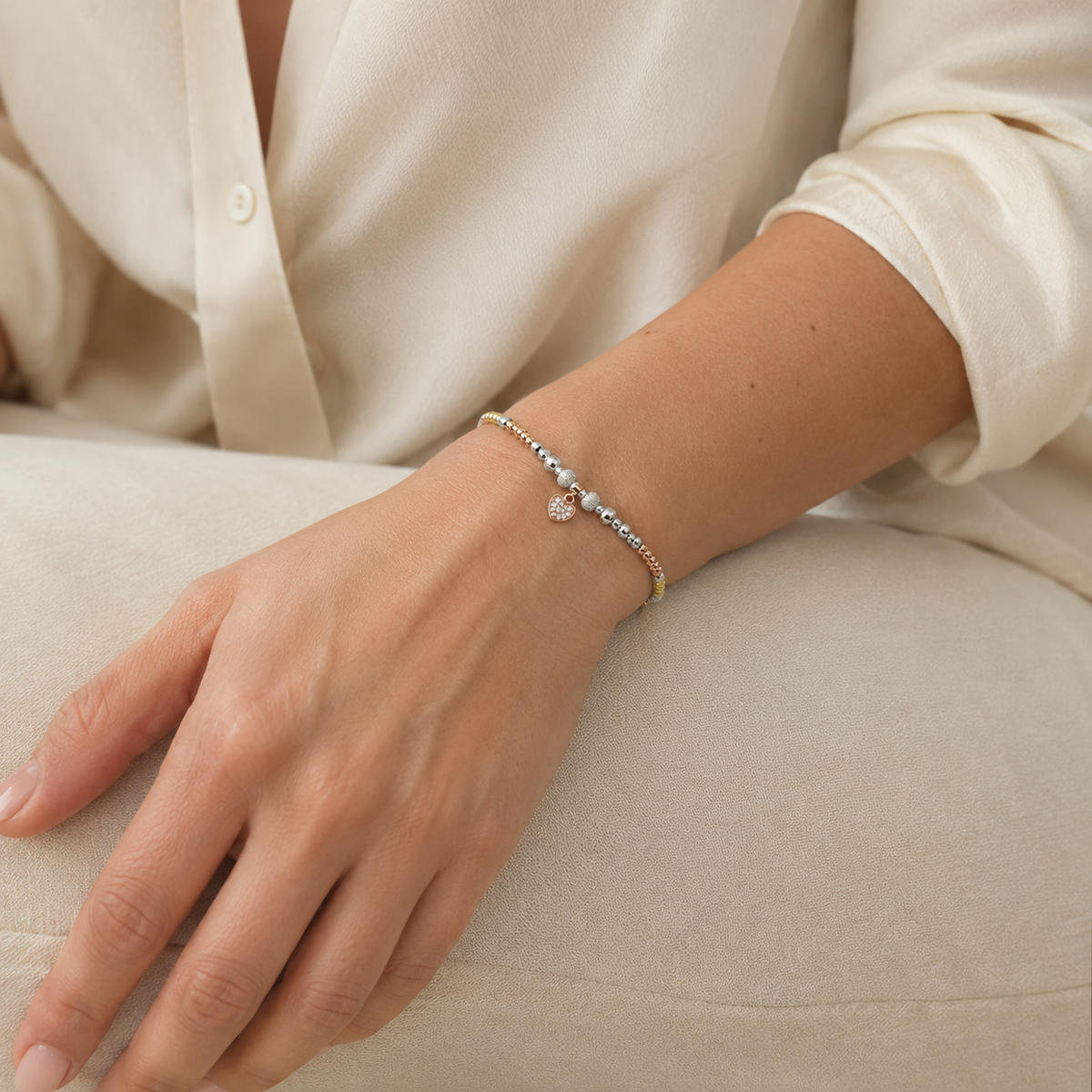 A mixed-metal heart bracelet with polished beads and a small charm.