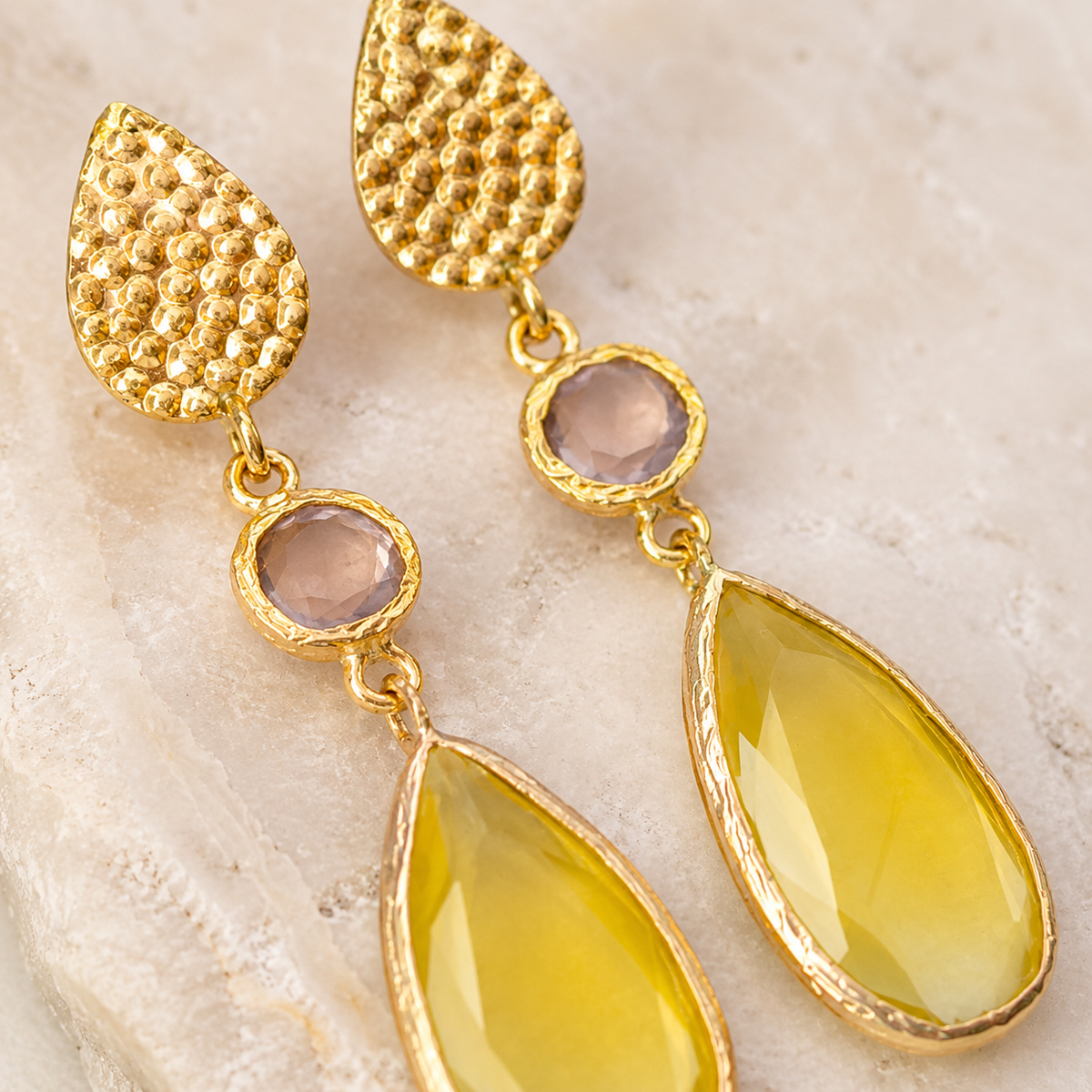 Close view of hammered gold-plated earrings with faceted round accents and teardrop drops.