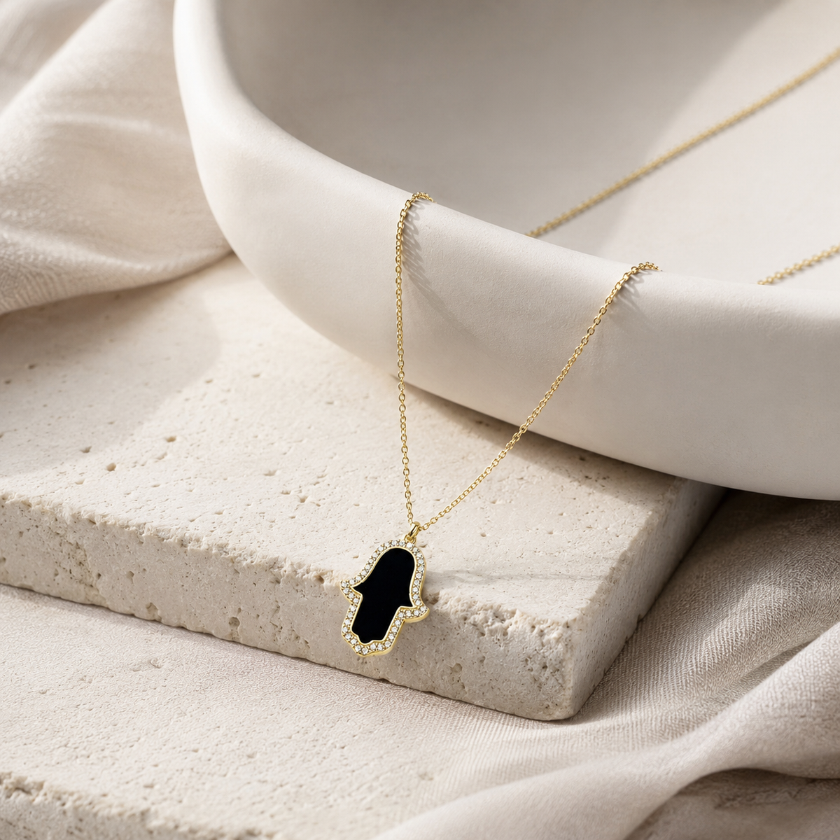 Angled view of a black enamel hamsa hand necklace with a gold-tone chain.
