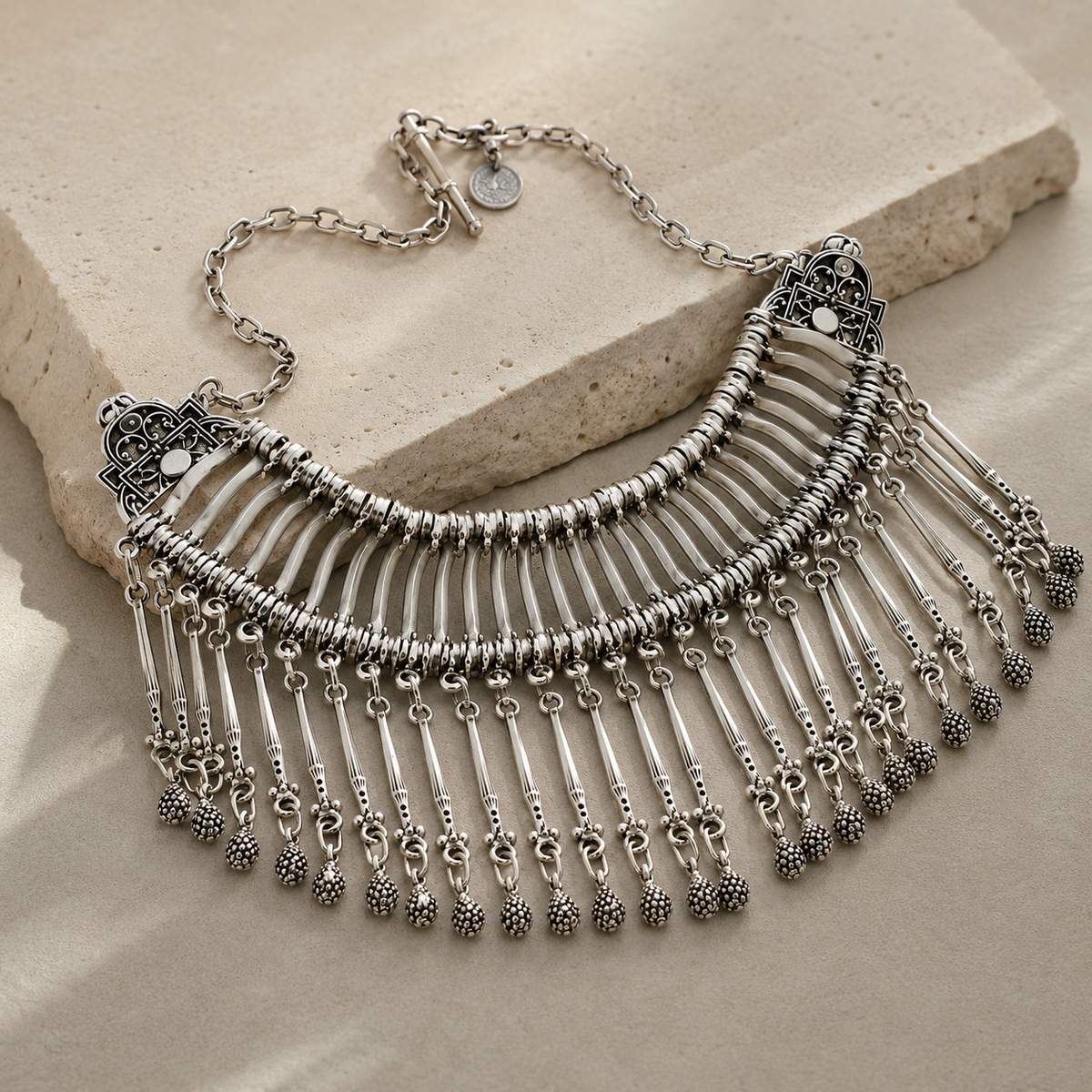Angled view of a silver chain fringe bib necklace with textured accents.