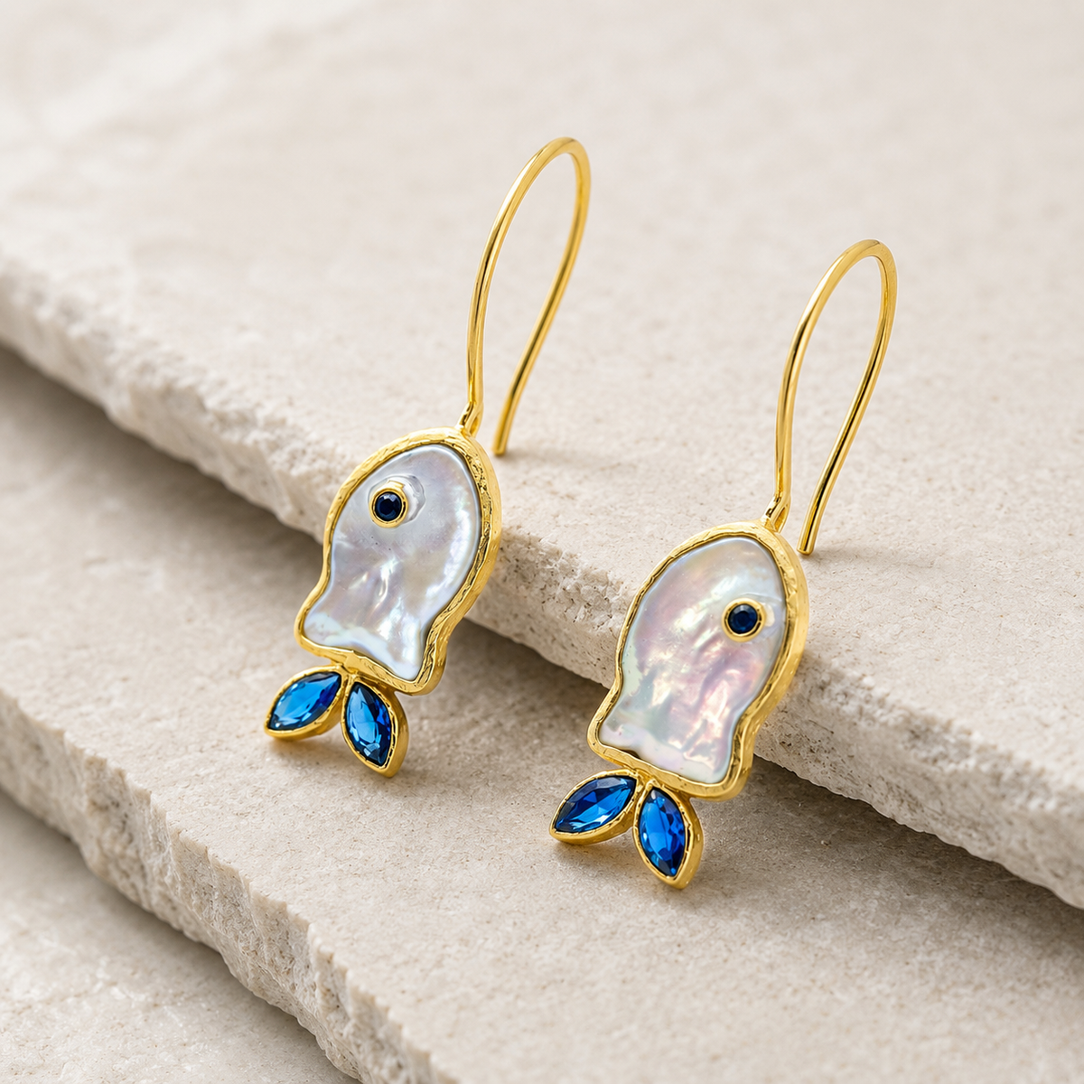 Side view of gold-plated hook earrings with mother-of-pearl fish shapes and blue CZ accents.