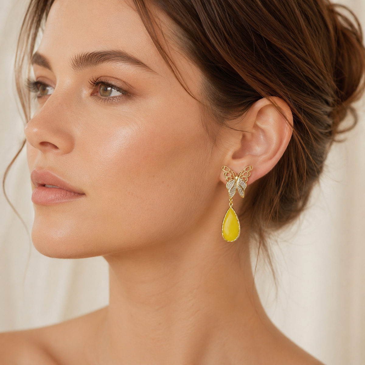 Gold butterfly drop earrings shown on a model with a long teardrop design.