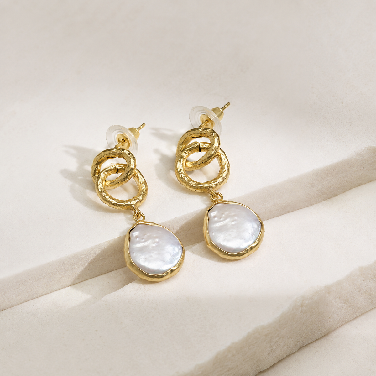 Angle view of gold plated drop earrings with chain links and pearl-inspired accents.