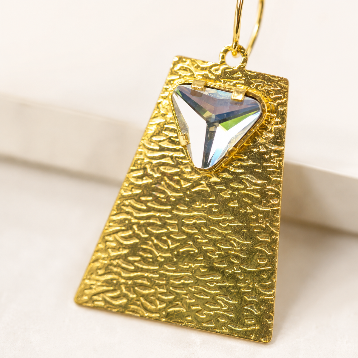 Close view of a clear crystal accent set in textured gold-plated earrings.