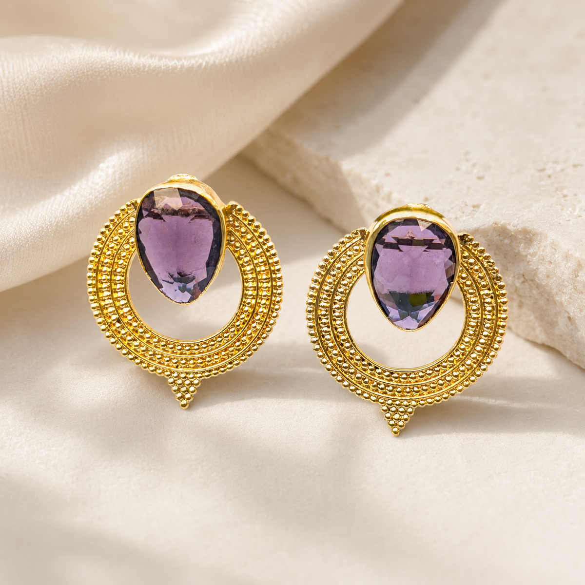 Gold-plated earrings with purple CZ stones and detailed circular edges.