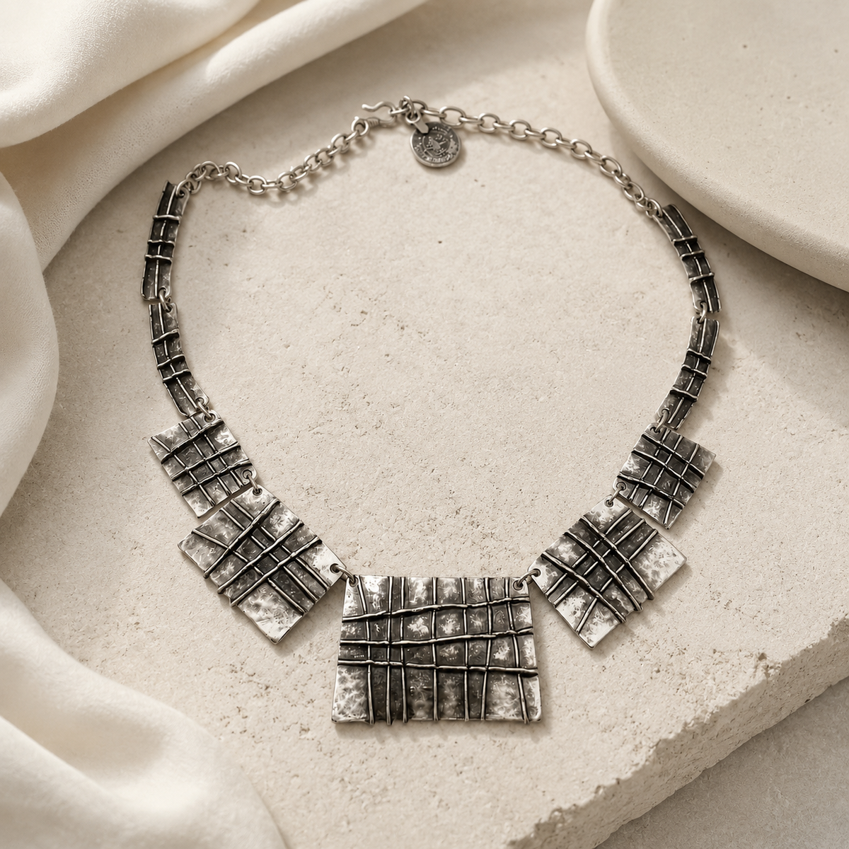 Silver-tone necklace with sculptural plaque shapes and a textured finish.