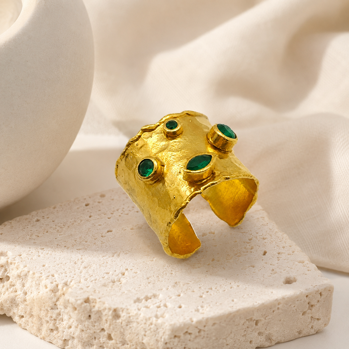 Gold cuff ring with emerald green stones styled as a bold statement piece.