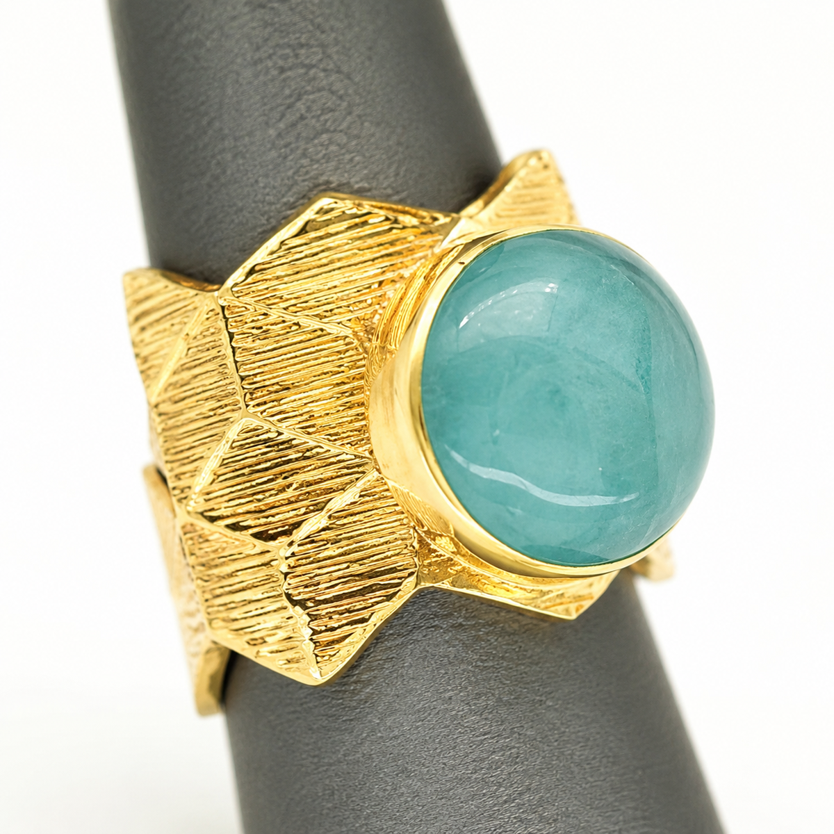 Close-up of the textured geometric gold-plated band and aqua blue round center.