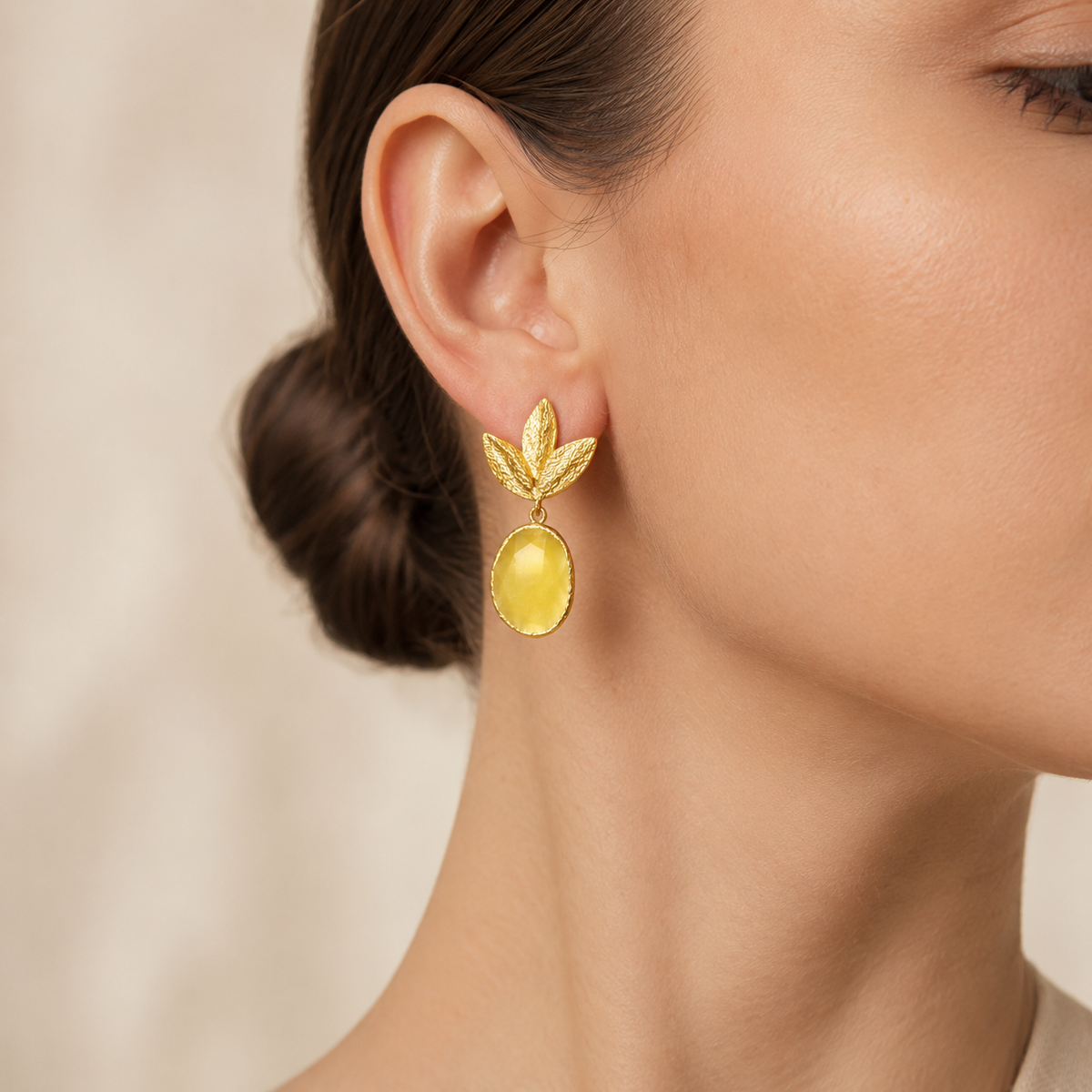 Gold plated leaf drop earrings with a mustard yellow stone-like oval accent.