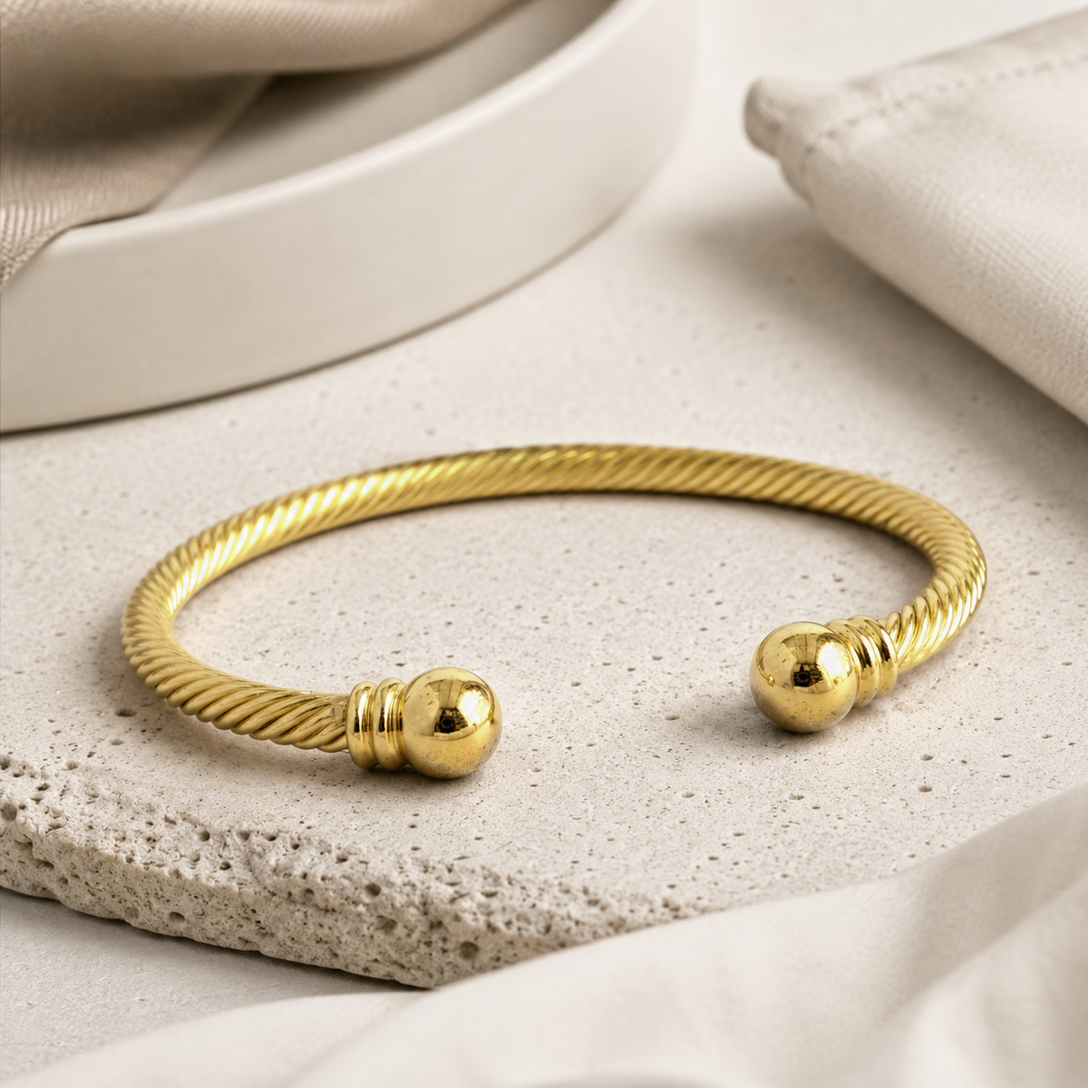 Angled view of a twisted gold-tone cuff bracelet with ball ends.
