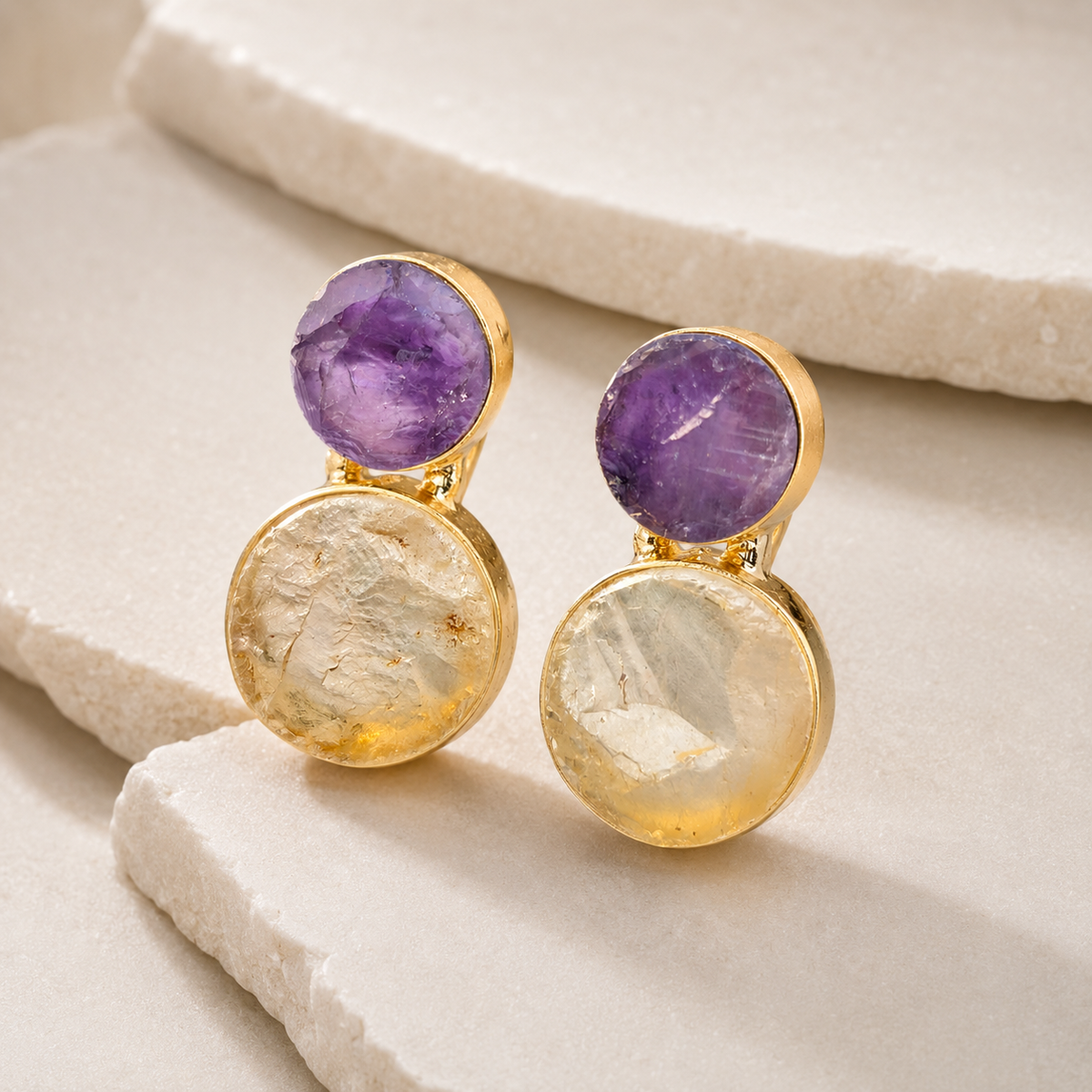 Angle view of layered drop earrings with purple amethyst and clear quartz stones.