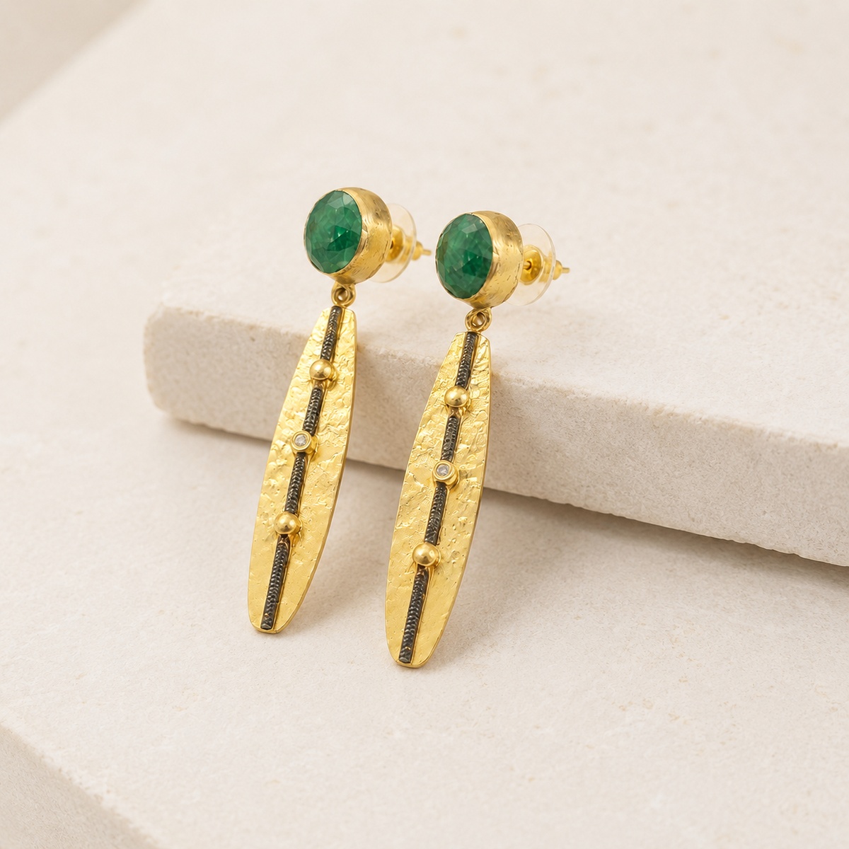 Angle view of gold-plated drop earrings with green stone tops.