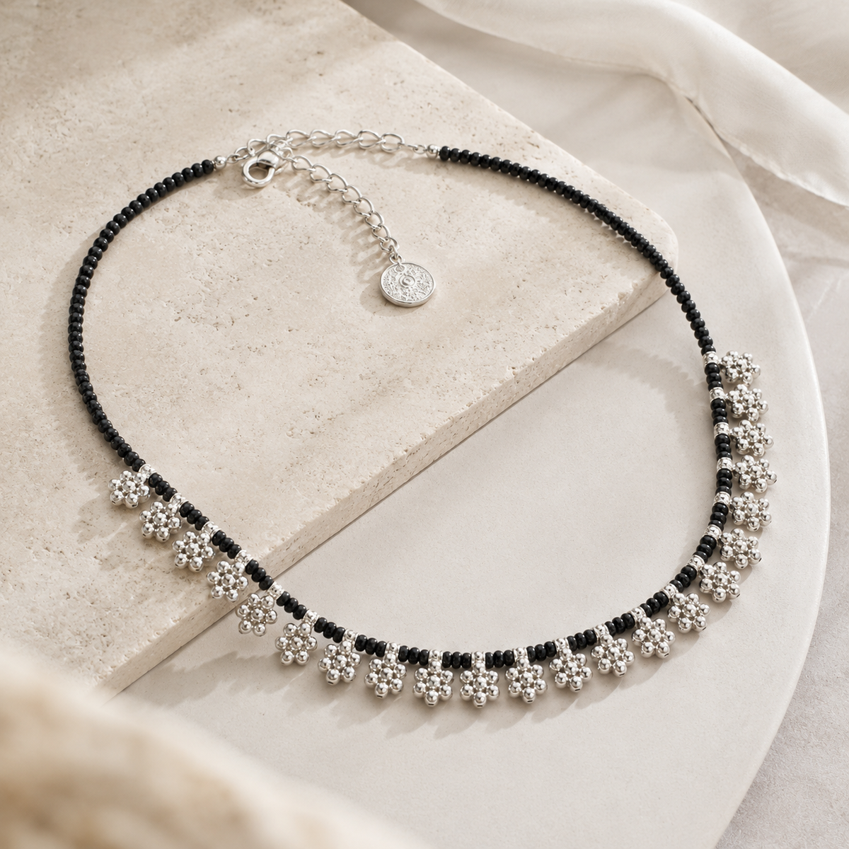 Angled view of a black bead floral fringe necklace with silver-tone details.