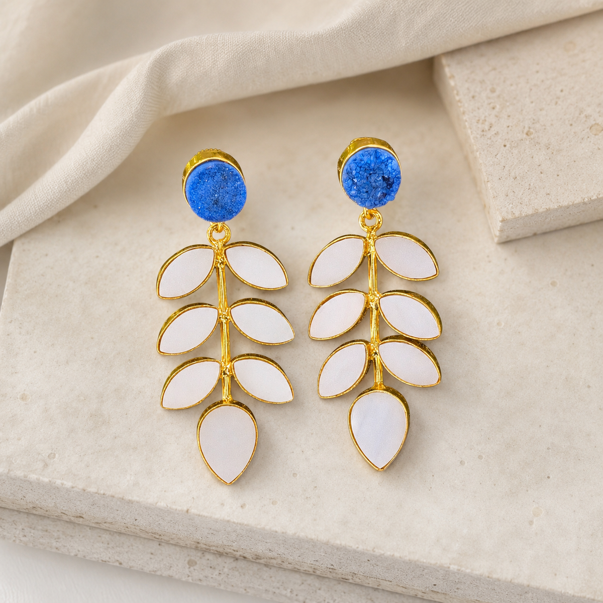 Gold-plated leaf drop earrings with blue druzy tops on a white background.