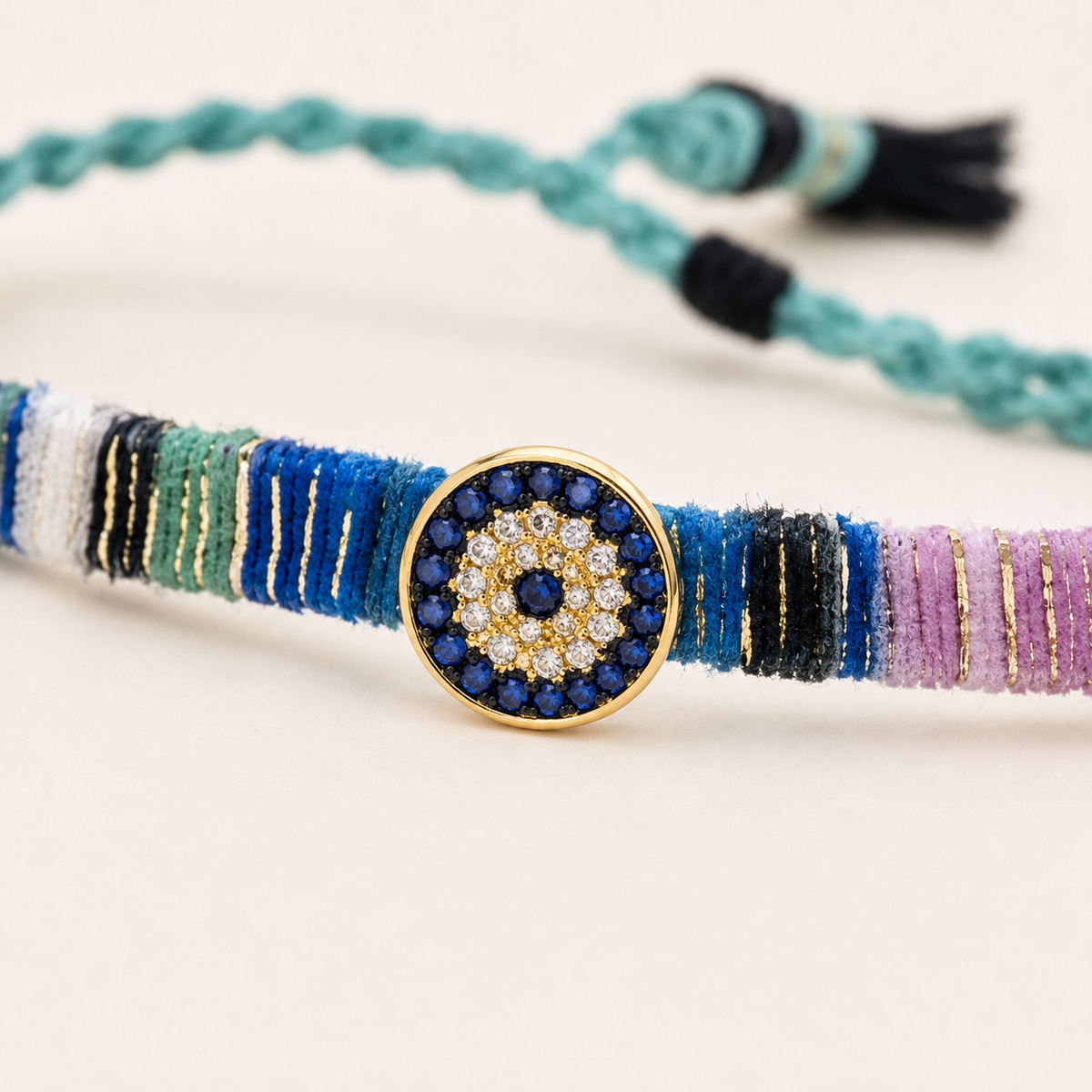 Close view of the jeweled evil eye centerpiece on a multicolor fabric bracelet.