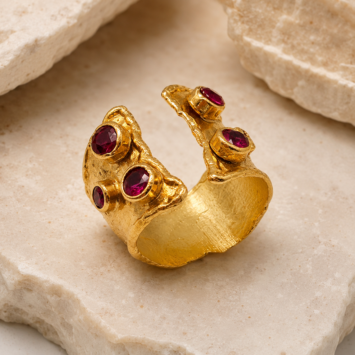 Angled view of a gold-plated open cuff ring with ruby pink stones.