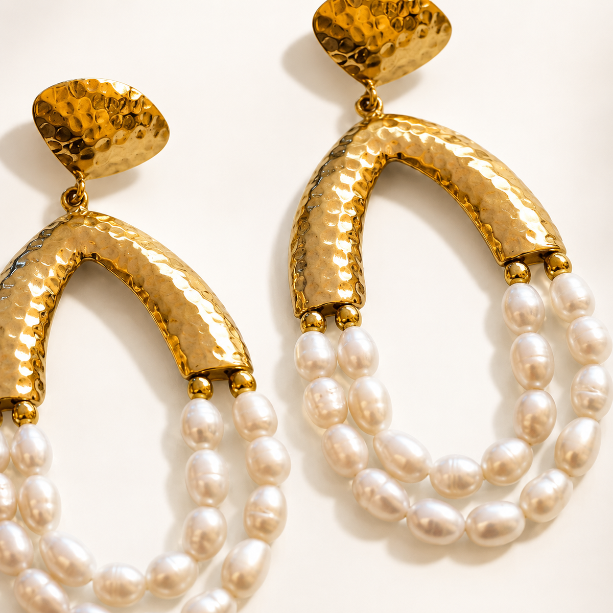 Close view of gold-tone hammered arches and pearl drop details on chandelier earrings.
