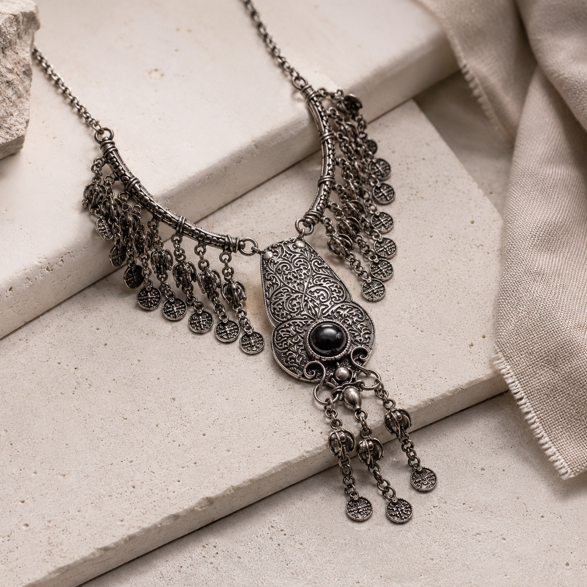 Angled view of a silver-tone filigree pendant necklace with dangling coin charms.