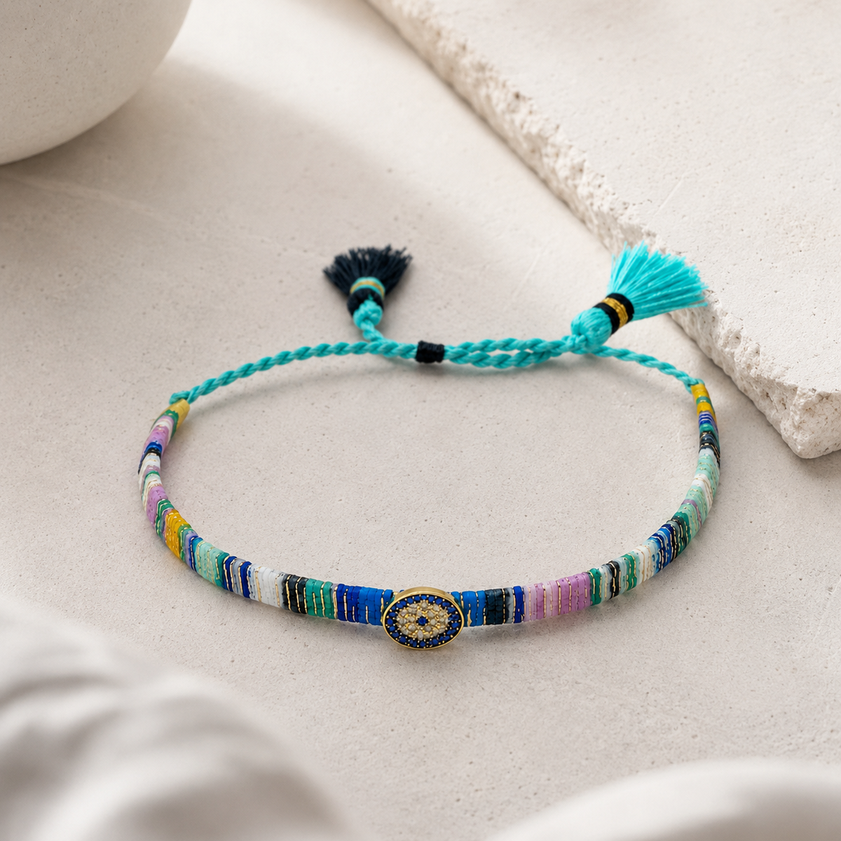Angled view of a colorful woven bracelet with tassel ties and evil eye center detail.