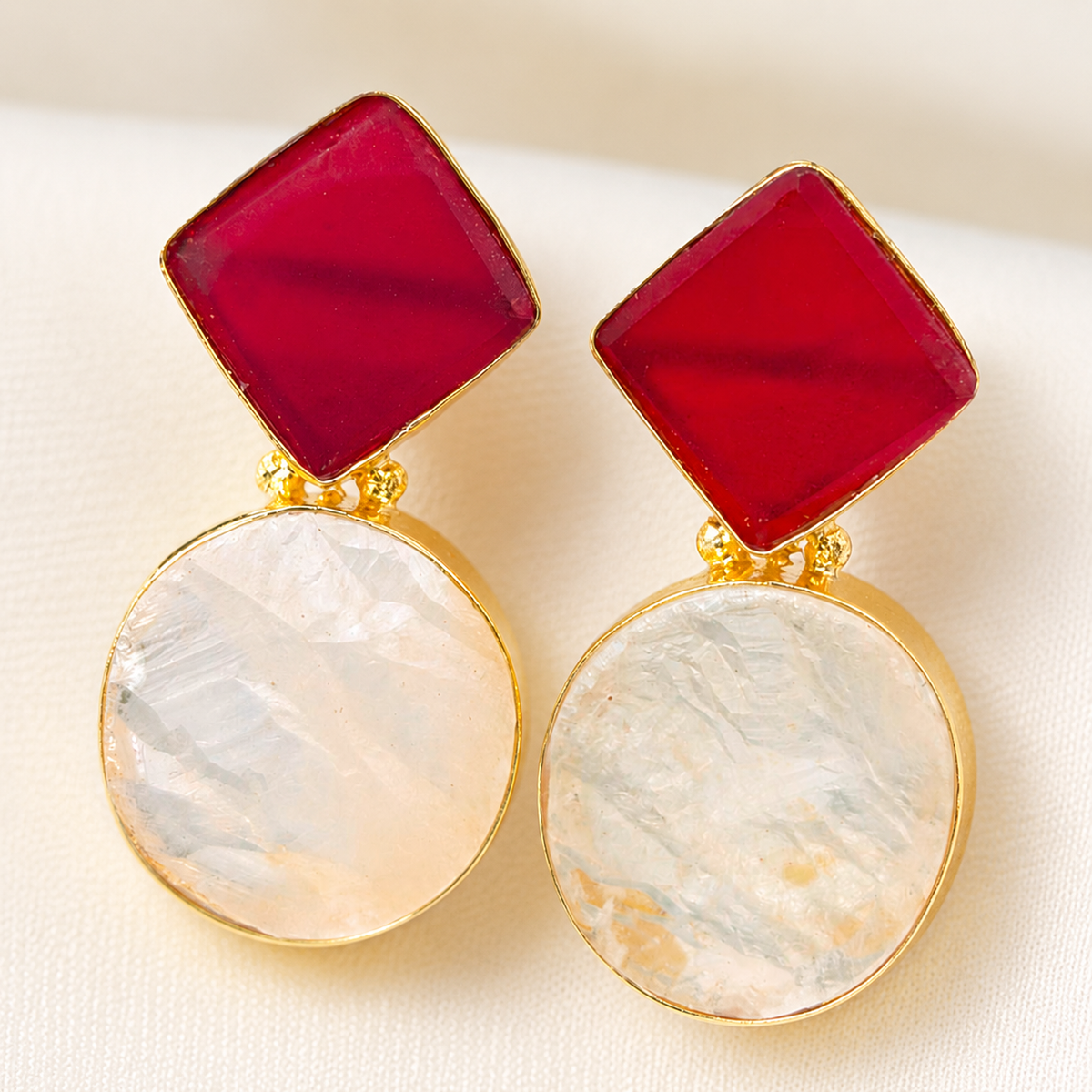 Close view of red geometric stones and clear quartz-like drops in gold-tone settings.
