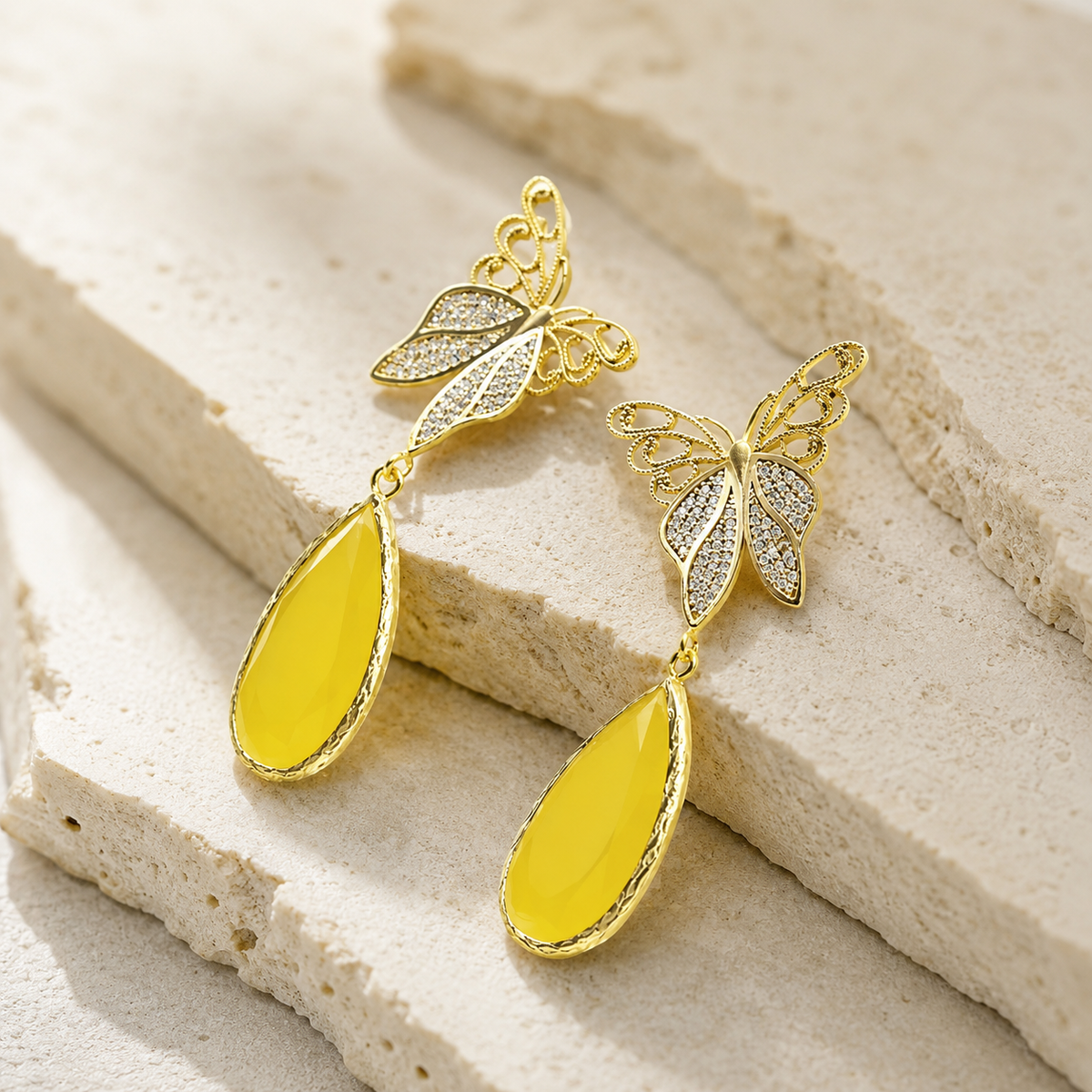 Angle view of gold butterfly drop earrings with a bright teardrop shape.