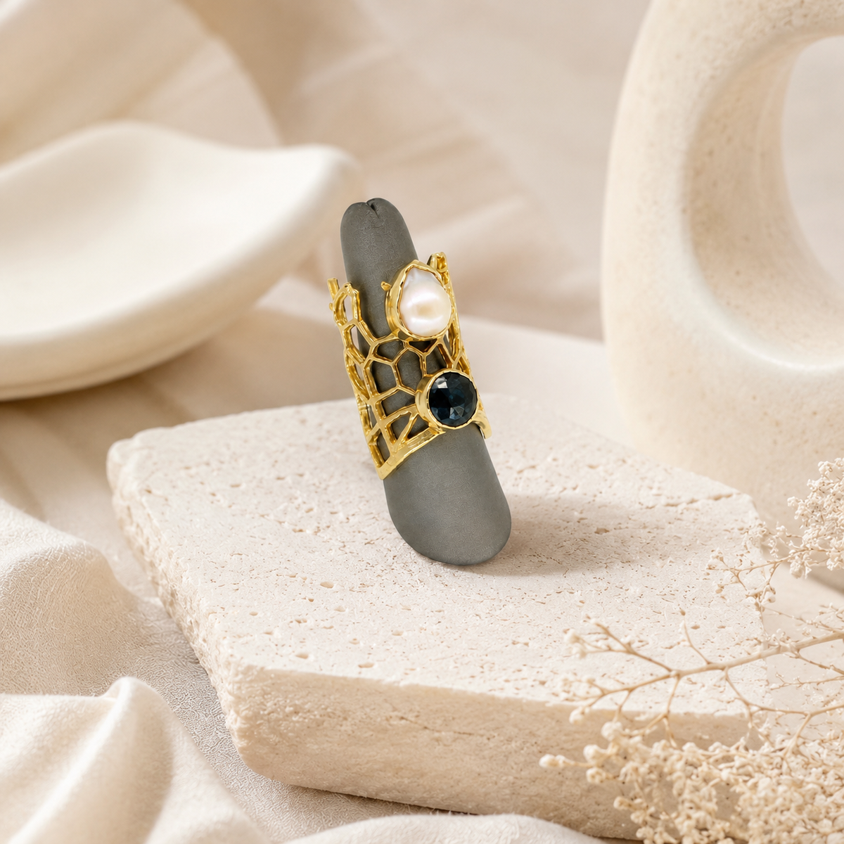Gold-plated statement ring with open honeycomb detailing and contrasting pearl-like and dark stones.