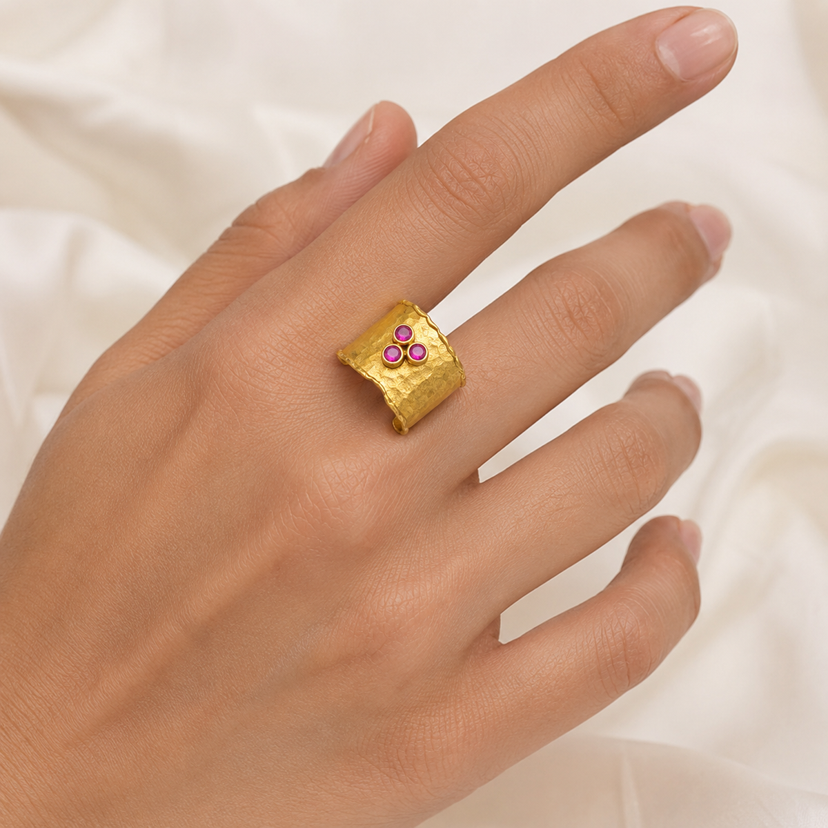 Hammered gold-plated cuff ring with three ruby pink stones on a white background.
