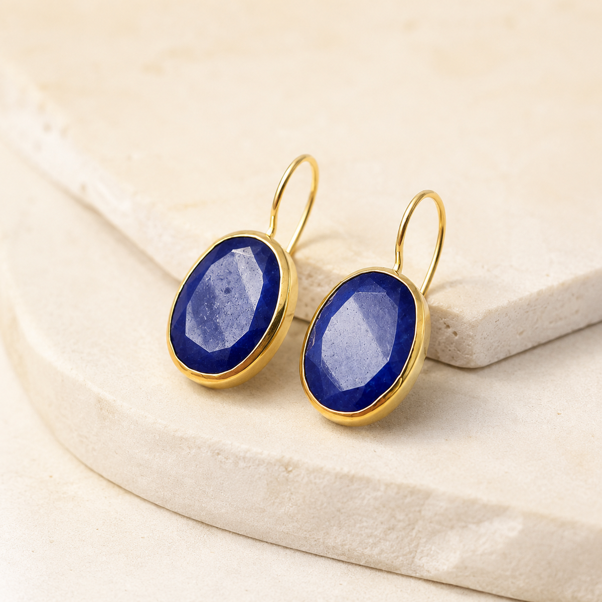 Angled view of gold-plated drop earrings with deep blue faceted oval stones.