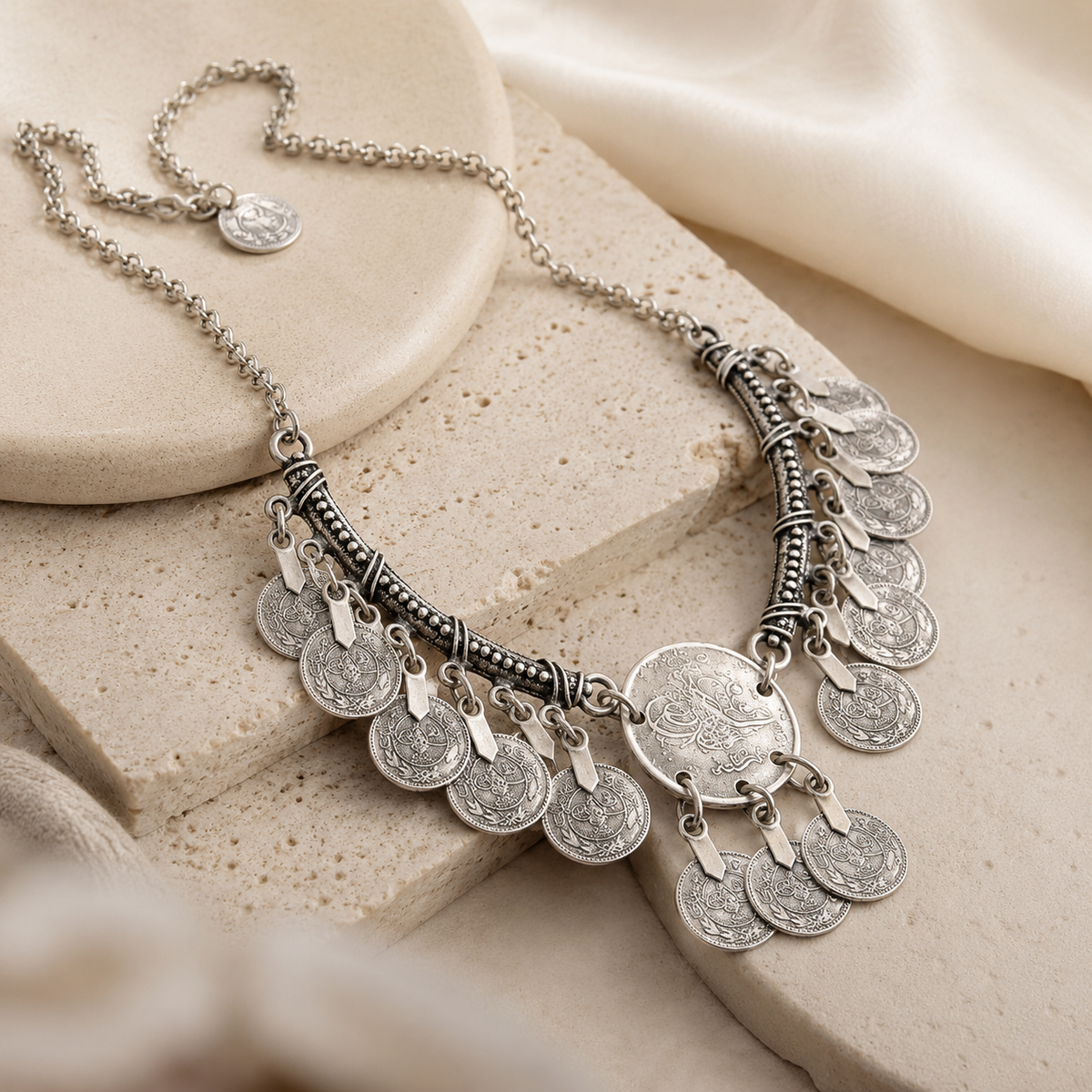 Angled view of a silver-tone crescent pendant necklace with layered coin fringe.
