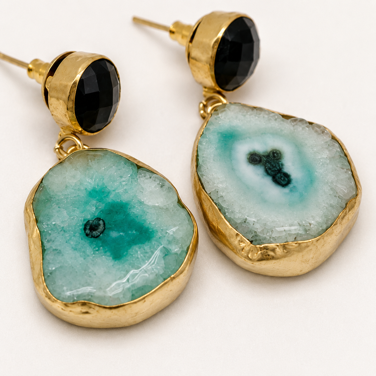 Close view of gold-plated earrings showing the faceted black top and organic stone drop.